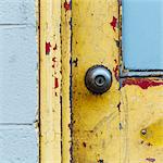 A doorway and the doorbell of a building. Flaked damaged paint.