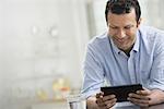 A man in a blue shirt leaning on a desk, holding a digital tablet.