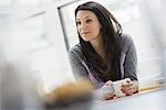 An office or apartment interior in New York City. A young woman with long black hair, having a cup of coffee.