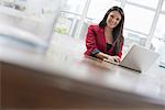 Business people. The office in summer. A young woman sitting comfortably in a quiet airy office environment. Using a laptop.