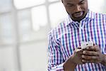 Professionals in the office. A light and airy place of work. A man in a checked shirt using a smart phone.