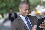 Business people in the city. Keeping in touch on the move. Two men in the park, one using a digital tablet, and one checking a smart phone.