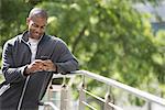 Business people in the city. Keeping in touch on the move. A man in a sweatshirt, leaning on a railing in the park, looking down at his smart phone.