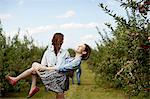 Rows of fruit trees in an organic orchard. Two young women laughing, one carrying the other.