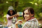 Two young woman drinking a toast at a picnic site or campsite in the woods.