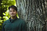 A man standing by a large tree with gnarled ridged bark.