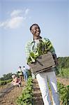 A boy holding a large wooden box of fresh vegetables, harvested from the fields.