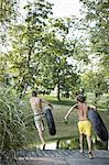 Two boys, leaping from the jetty into the water holding swim floats.