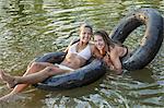 Two girls swimming and floating using swim floats and inflated tyres.