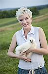 A young girl, teenager, holding a chicken with white feathers in her arms.