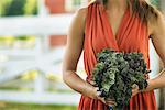 A woman holding a bunch of fresh picked vegetables, at a traditional farm.