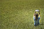 View from above of a woman sitting on grass, lifting up a personal computer notepad, looking at an image.