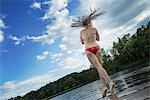 A young girl standing on tiptoes on the edge of a wooden jetty with her hair fanning out behind her, in motion.