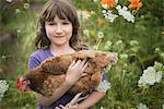 A young girl holding a domestic hen, with brown feathers and a red comb.