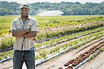 A man with arms folded, standing in a field, full of fresh salad and vegetable crops and flowers.