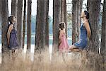 A group of people communing with nature, and leaning against tall straight trees in woodland.