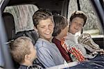 Four boys sitting in a car or truck, in a row.