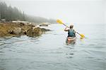 A man paddling a kayak on calm water in misty conditions. New York State, USA