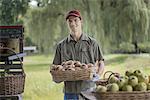 Organic farmer, young man holding baskets of fresh fruit at a market farm stand.