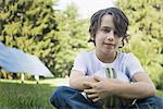 A boy holding a football, sitting on the grass. Solar panels.