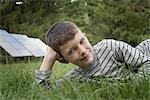 A boy lying in the grass, beside solar panels.