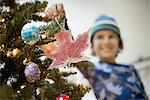 A young boy holding Christmas ornaments and placing them on the Christmas tree.