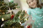 A young girl placing a homemade Christmas ornament on a tree.