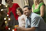 A Christmas gathering, adults and children in a room around a Christmas tree, celebrating together.
