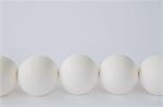End-on view of free range, organic eggs with white shells arranged in a row, on a white background.