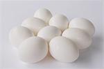 A small group or clutch of nine free range organic egg with white shells against a white background.