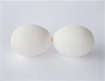 Two free range organic eggs with white shells, end to end, against a white background.