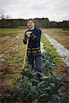 Organic Farmer at Work. A young man leaning on a long handled garden hoe, among the crops.