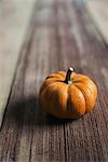 A small round pumpkin or squash vegetable with a bright orange skin, on a wooden tabletop.