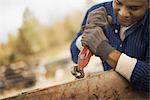 A man working in a reclaimed timber yard. Using a tool to remove metals from a reclaimed piece of timber.