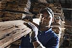 A heap of recycled reclaimed timber planks of wood. Environmentally responsible reclamation in a timber yard. A man carrying a large plank of splintered rough wood.