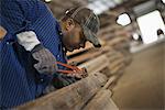 A man working in a reclaimed timber yard. Using a tool to remove metals from a reclaimed piece of timber. Workshop.