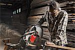 A reclaimed lumber workshop. A man in protective eye goggles using a circular saw to cut timber.