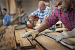 A reclaimed lumber workshop. A group of people working. A man measuring and checking planks of wood for re-use and recycling.