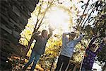 Three children in the autumn sunshine. Playing outdoors throwing the fallen leaves  in the air.