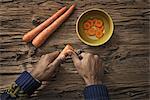 A person holding and slicing fresh carrots into a bowl.