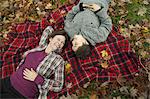 Two people, a woman and a child, lying on a red tartan picnic blanket, looking upwards.