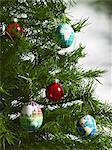 Still life. Green leaf foliage and decorations. A pine tree branch with green needles. Christmas decorations. A small group of red and blue tree ornaments. Oblong shapes with continents outlined on a blue background.