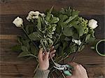 A woman holding secateurs and cutting the base of flower stems for a flower arrangement of white roses and green foliage.