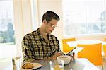 A young man in a coffee shop reading using a tablet computer.