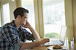 A young man sitting at a table using a laptop computer.