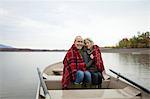 A couple, man and woman sitting in a rowing boat on the water on an autumn day. Sharing a picnic rug to keep warm.