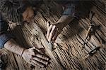 A man working in a reclaimed lumber yard workshop. Holding tools and sanding knotted and uneven piece of wood.