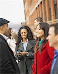 City life. A group of people on the go, keeping in contact, using mobile phones, and talking to each other. Men and women, five people outdoors.