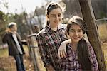 Two young girls beside a paddock fence, and a man in the background. An organic farm.