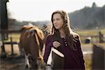 A girl leaning on a paddock fence, and a grazing horse in the background, on an organic farm.